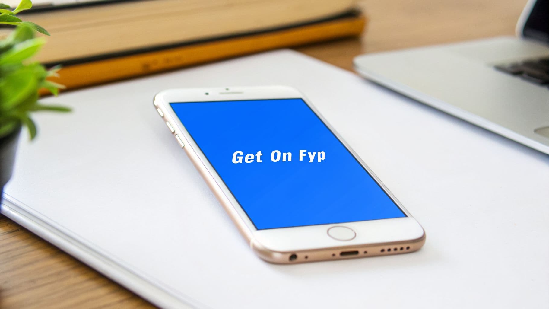 A white smartphone displaying "Get On Fyp" on its blue screen, on a desk with a laptop.