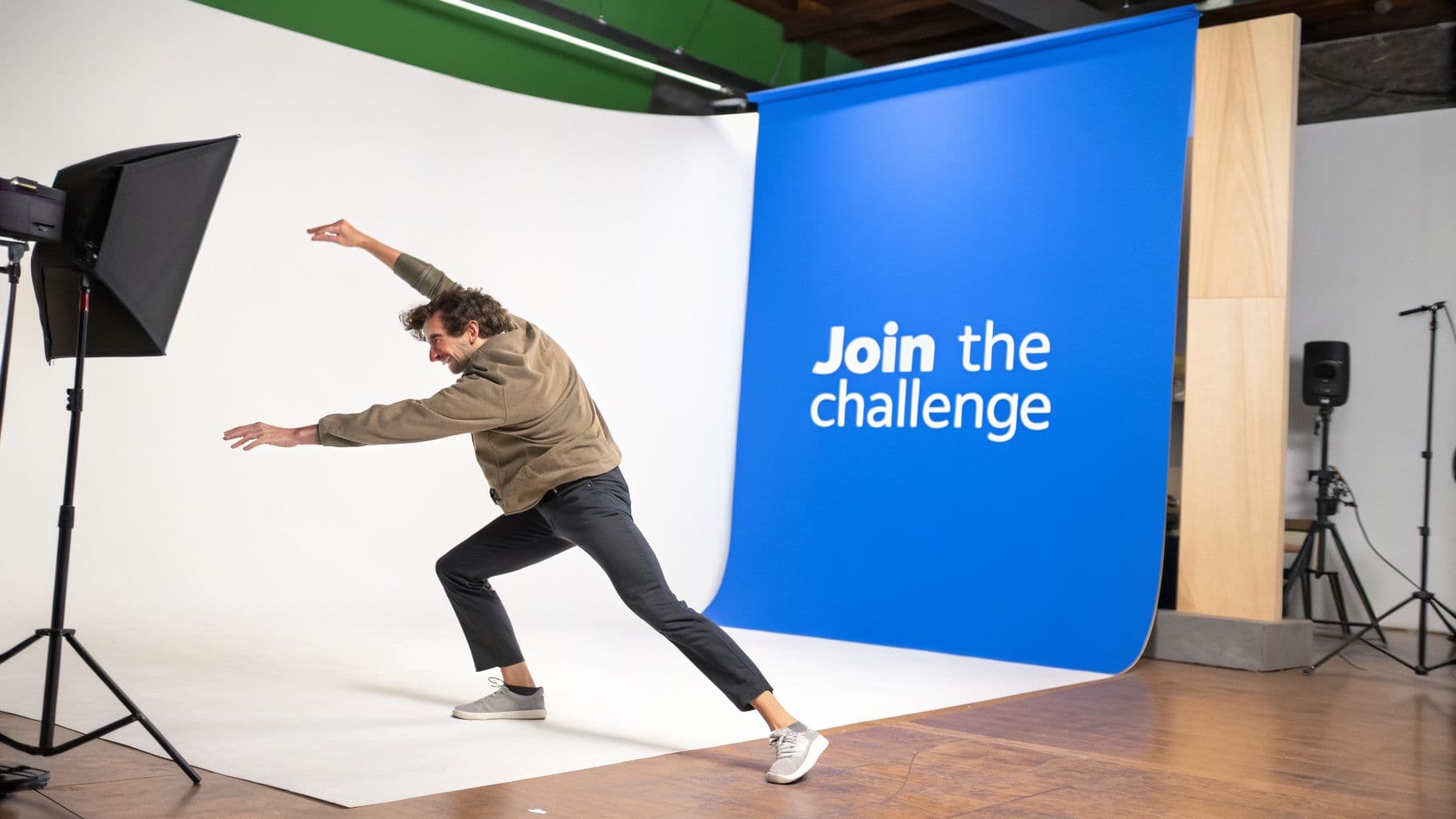 A man in a studio setting, posing dynamically in front of a blue backdrop that reads 'Join the challenge'.