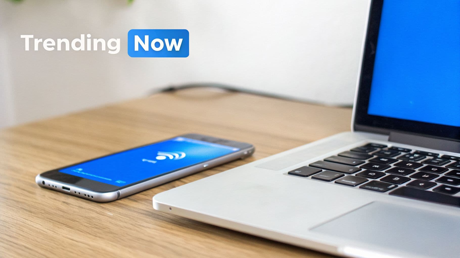 A laptop and smartphone on a wooden desk with a blue screen, featuring 'Trending Now' text overlay.