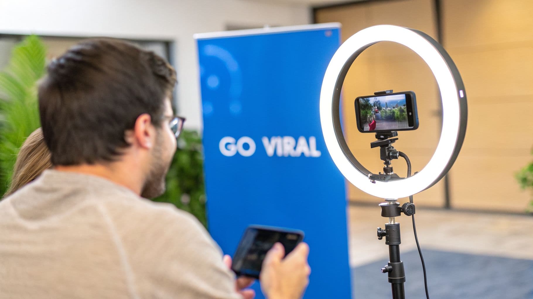 A person uses a smartphone attached to a ring light, facing a 'GO VIRAL' banner.
