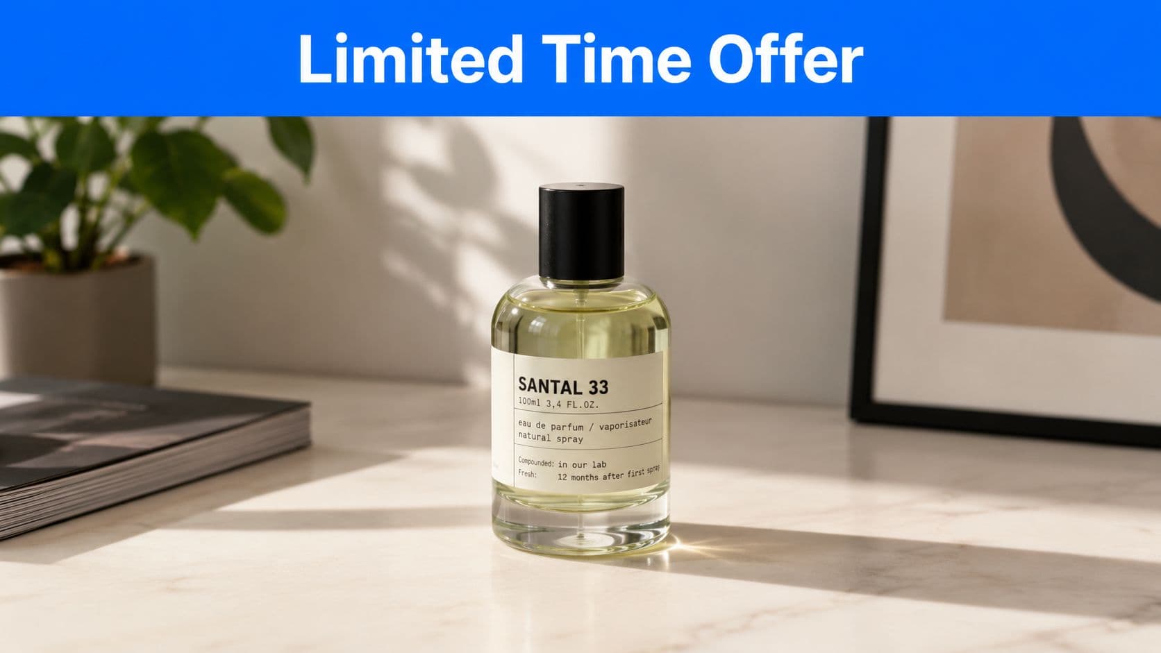 A glass bottle of Santal 33 perfume sits on a white marble table with a plant and frame.