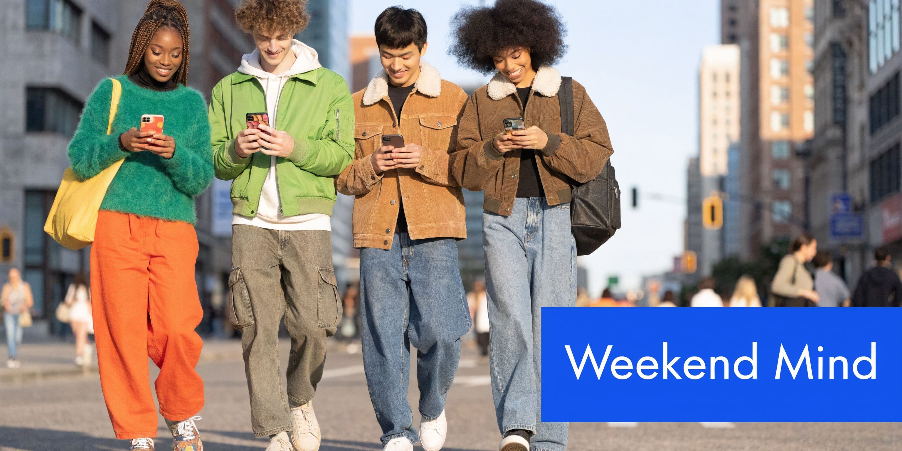 A group of four diverse young friends walking down a city street while looking at their smartphones.